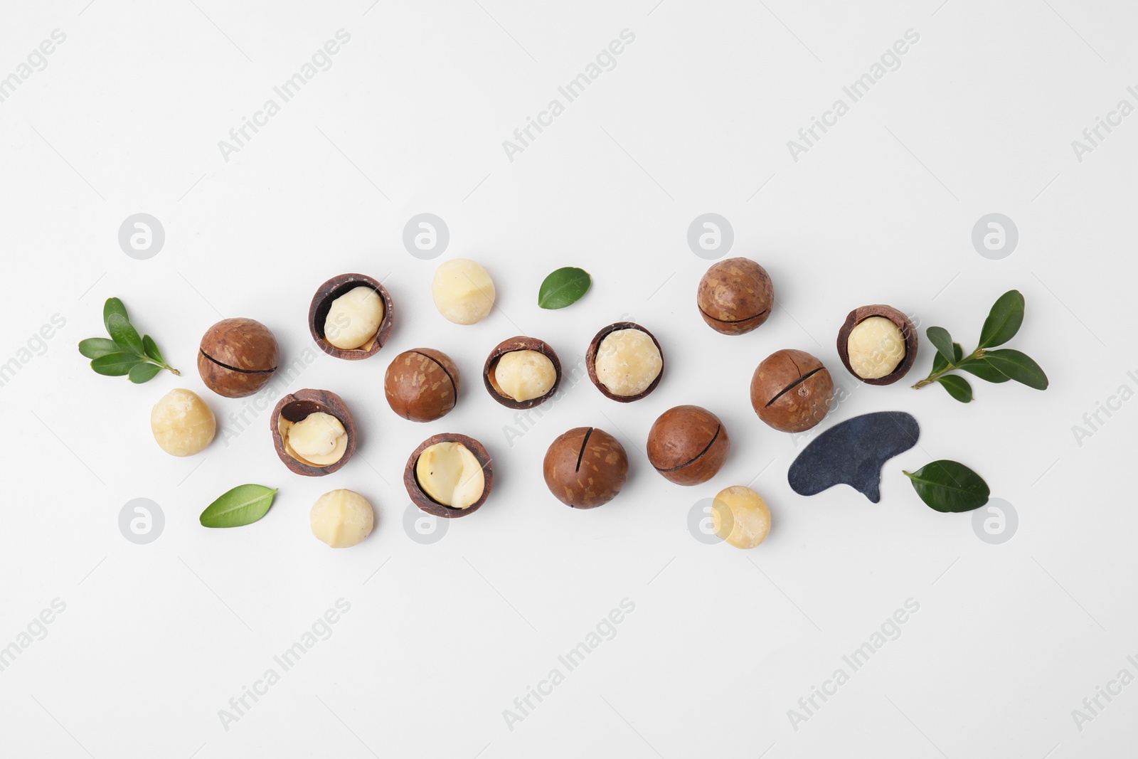 Photo of Tasty Macadamia nuts and green leaves on white background, flat lay