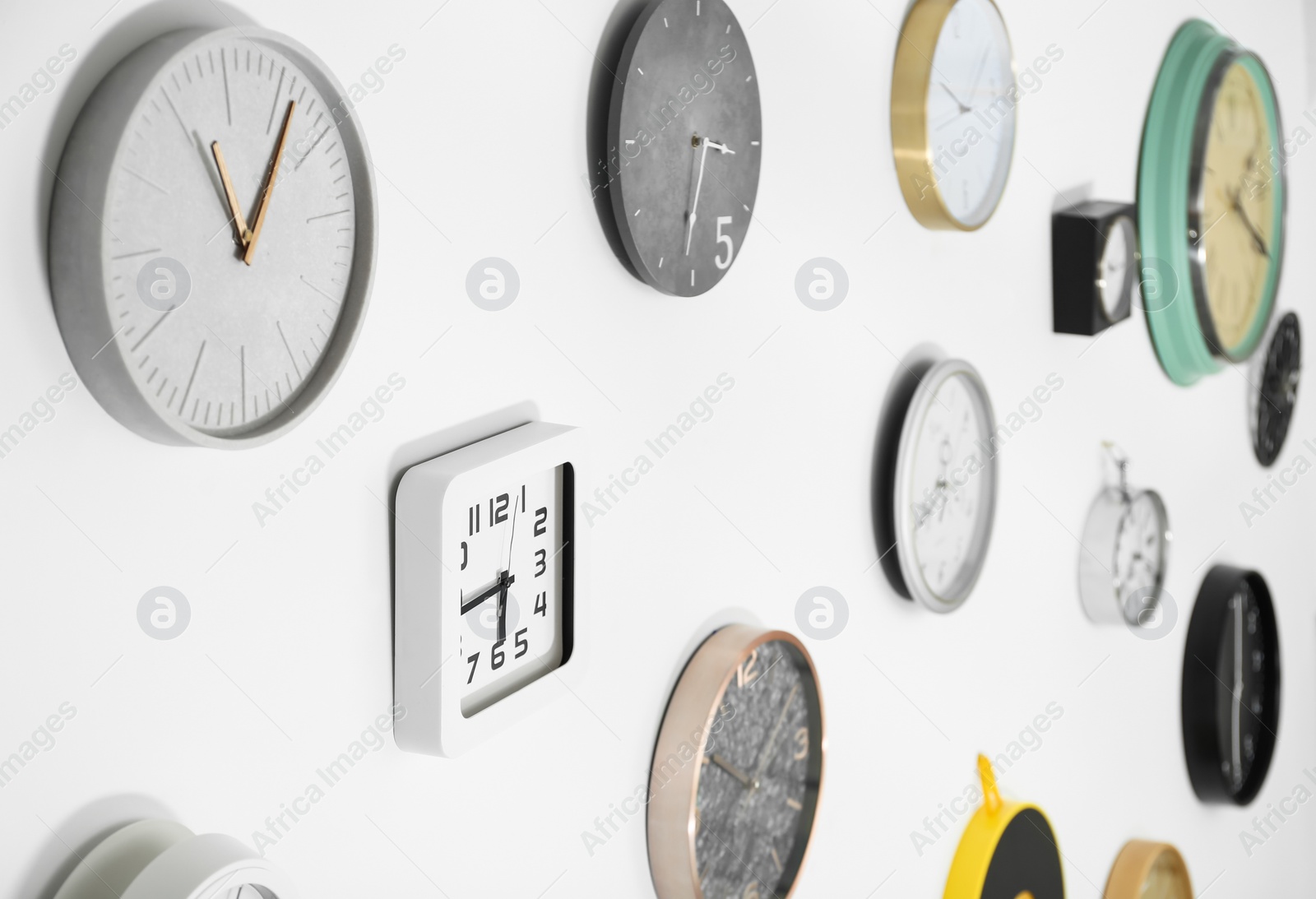 Photo of Many different clocks hanging on white wall. Time of day