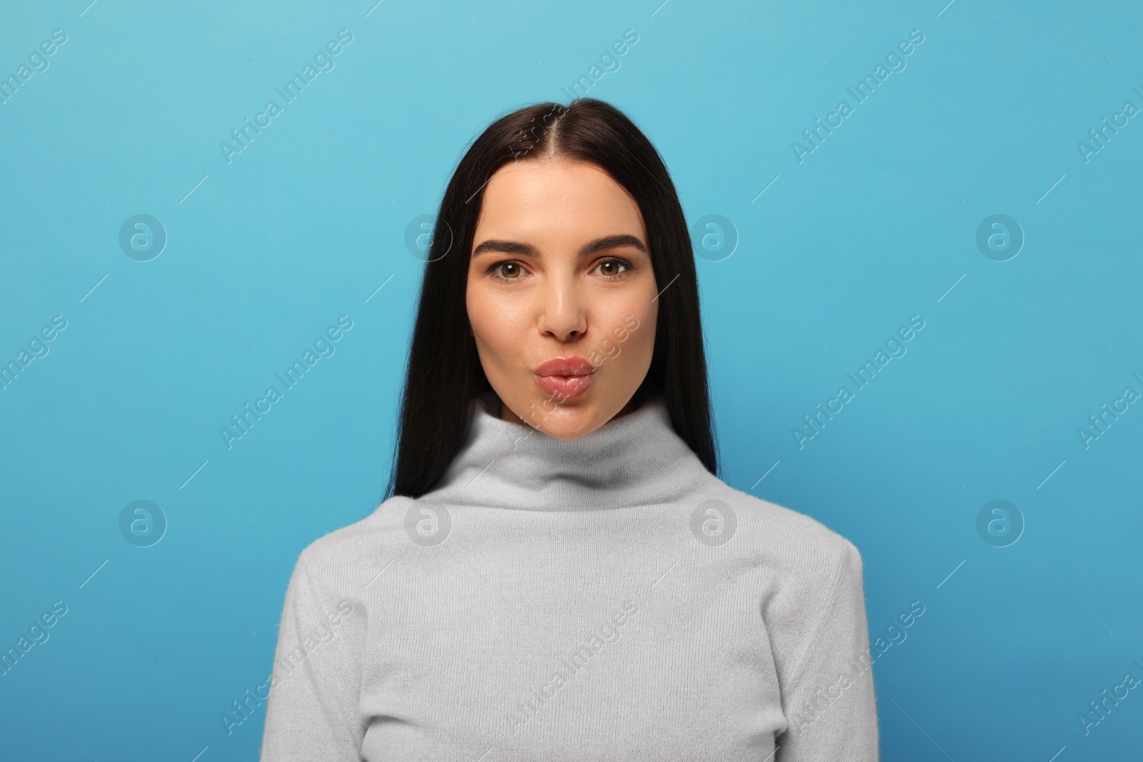 Photo of Beautiful young woman blowing kiss on light blue background