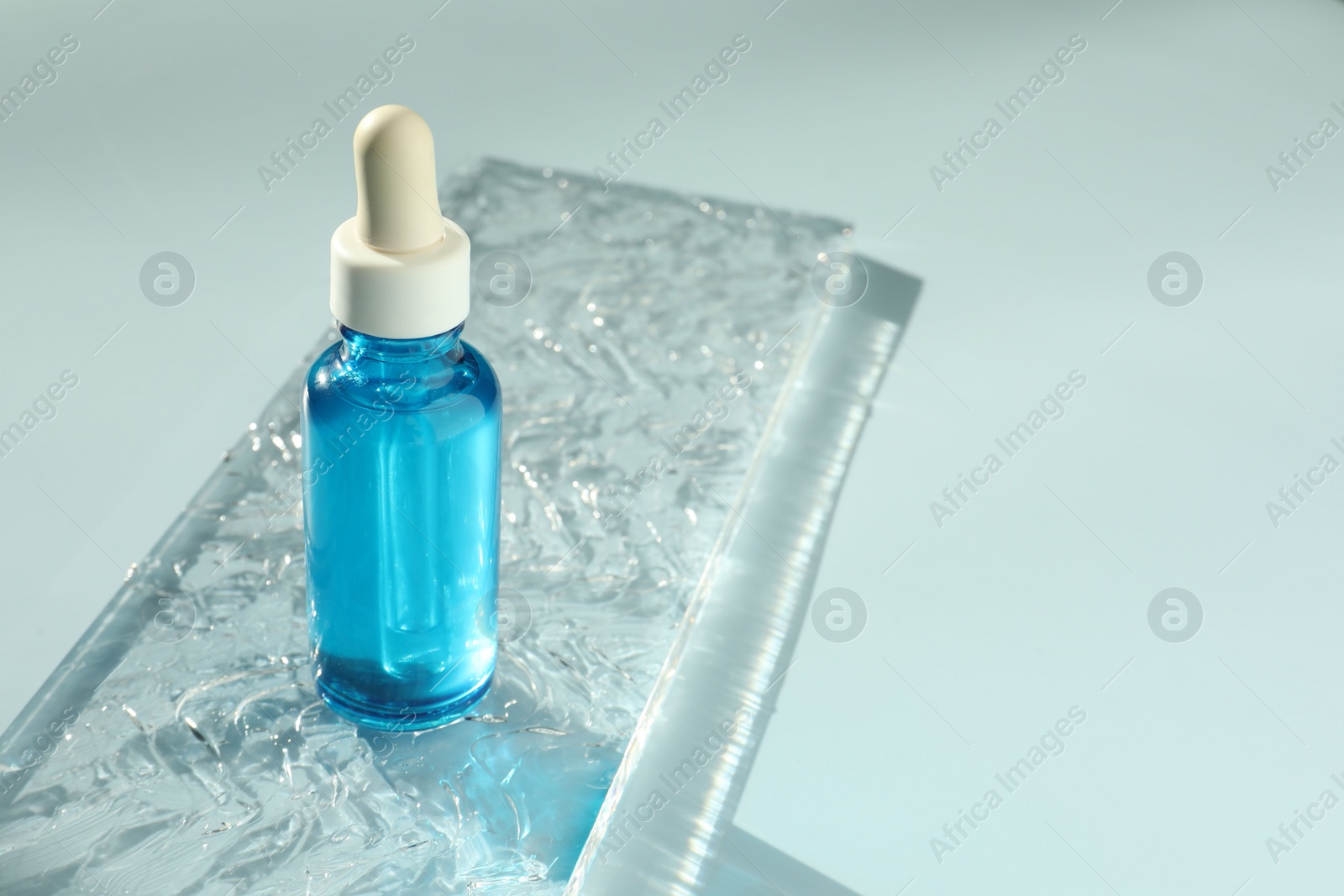 Photo of Bottle of cosmetic serum on light blue background, space for text