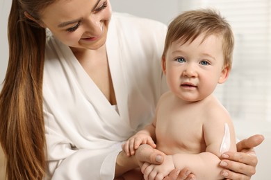 Happy mother applying body cream onto baby`s skin indoors