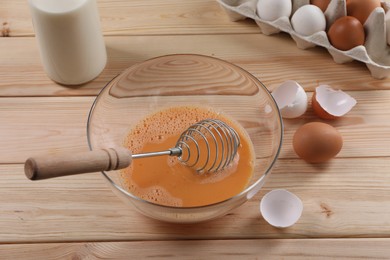 Photo of Making dough. Beaten eggs in bowl, shells and milk on wooden table, closeup