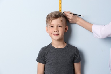 Photo of Doctor measuring little boy's height on light background