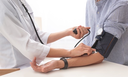 Photo of Doctor checking patient's blood pressure in hospital, closeup. Cardiology concept