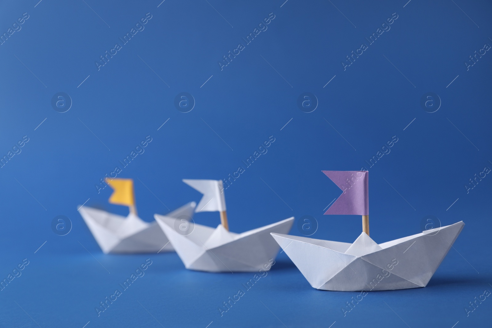 Photo of Handmade paper boats with flags on blue background. Origami art