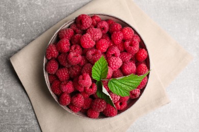Photo of Bowl of fresh ripe raspberries with green leaves on grey table, top view