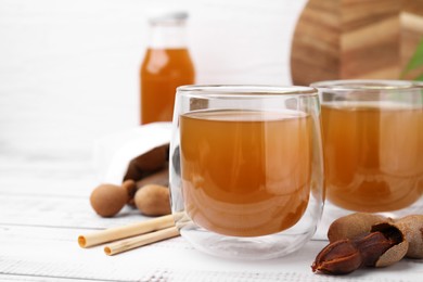 Photo of Tamarind juice and fresh fruits on white wooden table, closeup. Space for text