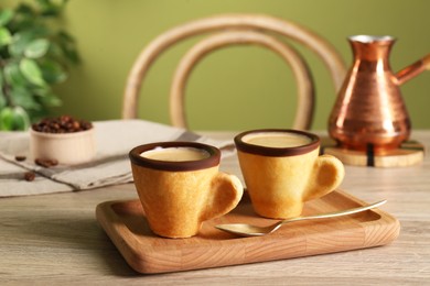 Photo of Delicious edible biscuit cups with coffee, spoon and board on wooden table