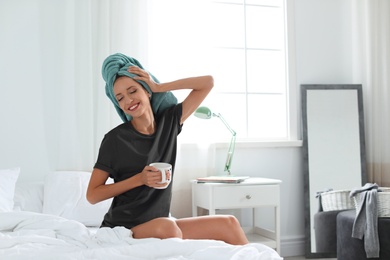 Young happy woman with cup of aromatic coffee on bed at home. Lazy morning