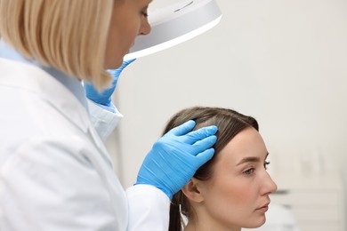 Photo of Trichologist examining patient`s hair under lamp in clinic, closeup