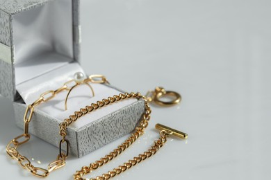 Photo of Metal chain and jewelry box with ring on white table, closeup. Space for text