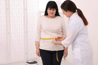 Photo of Nutritionist measuring overweight woman's waist with tape in clinic, space for text