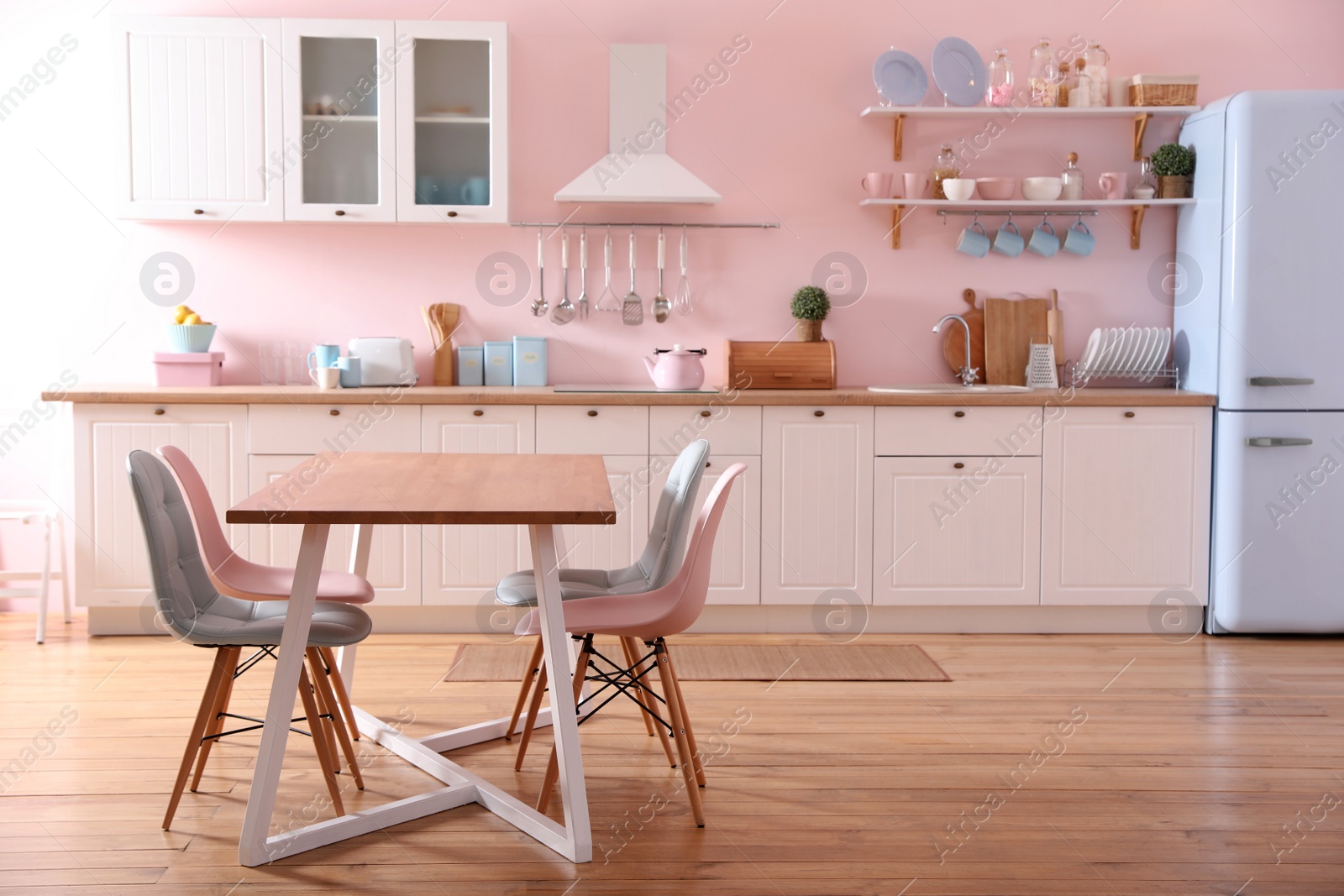 Photo of Stylish pink kitchen interior with dining table and chairs