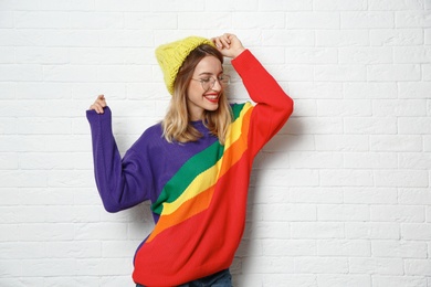 Beautiful young woman in warm sweater with hat near white brick wall. Space for text