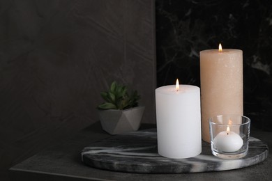 Photo of Marble board with burning candles on dark table, space for text