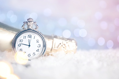 Photo of Pocket watch and bottle of champagne on snow against blurred lights, space for text. New Year countdown