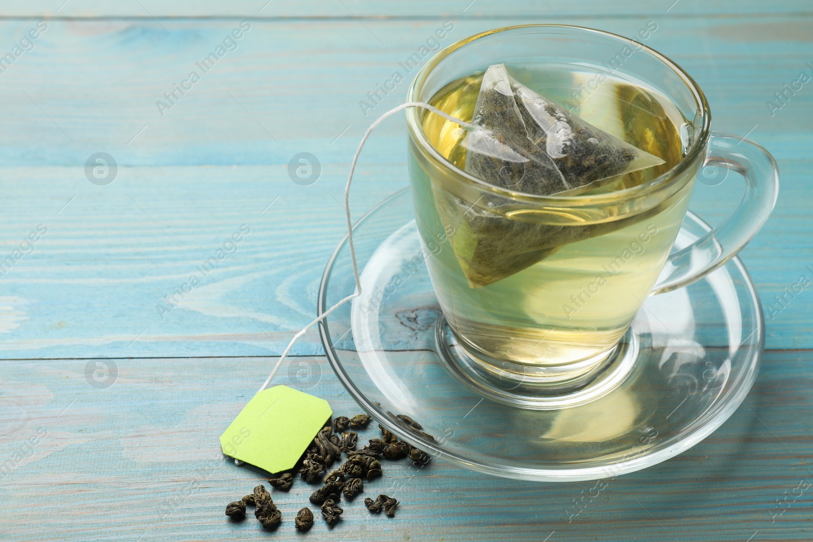 Photo of Tea bag in cup with hot drink and dry leaves on light blue wooden table, closeup. Space for text