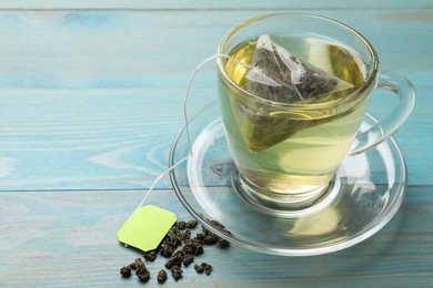 Tea bag in cup with hot drink and dry leaves on light blue wooden table, closeup. Space for text