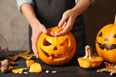 Woman making Halloween pumpkin head jack lantern on wooden table, closeup