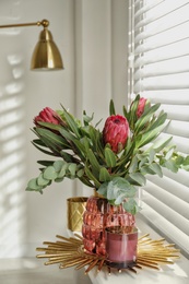 Vase with bouquet of beautiful Protea flowers on window sill indoors