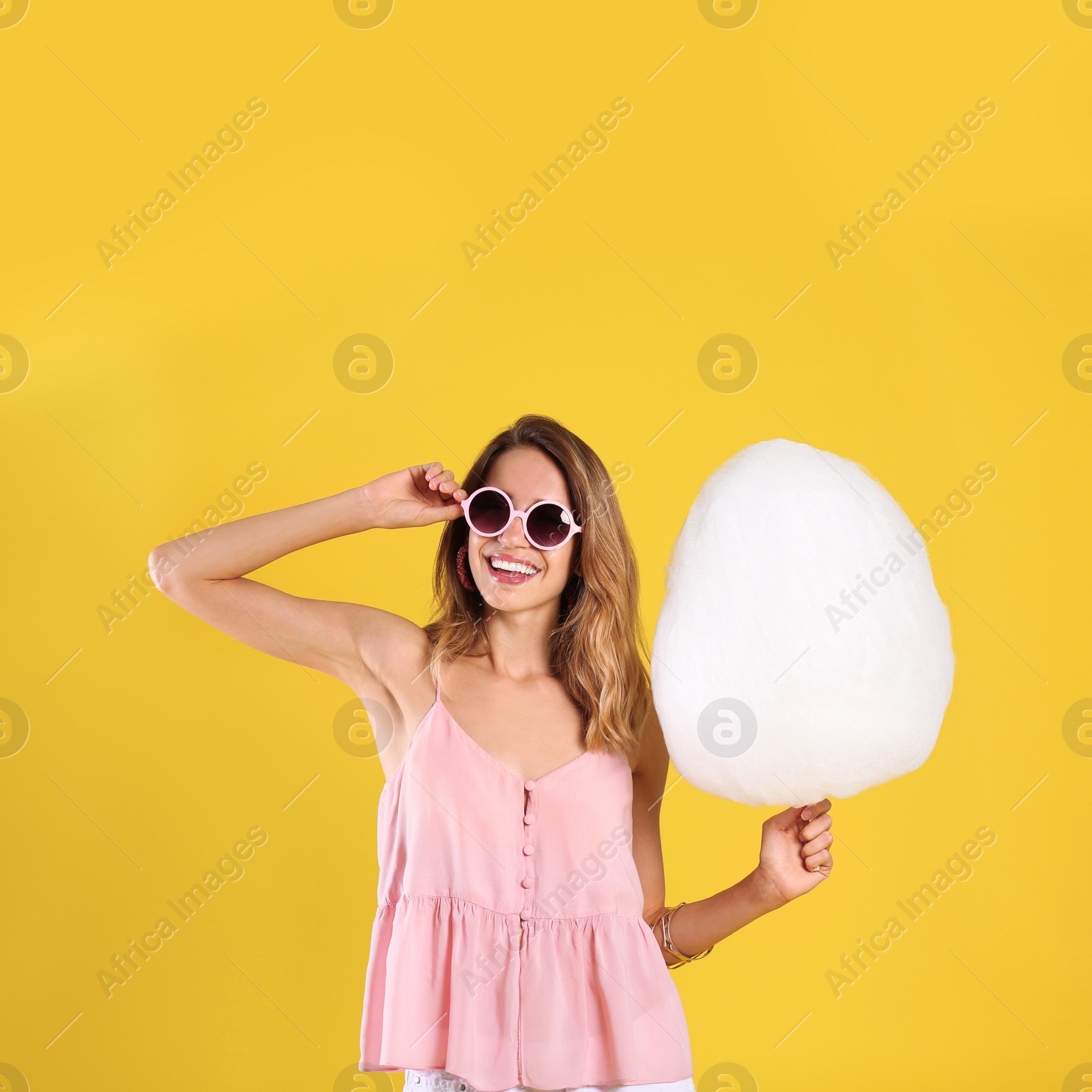 Photo of Happy young woman with cotton candy on yellow background