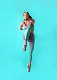 Athletic young woman running on turquoise background