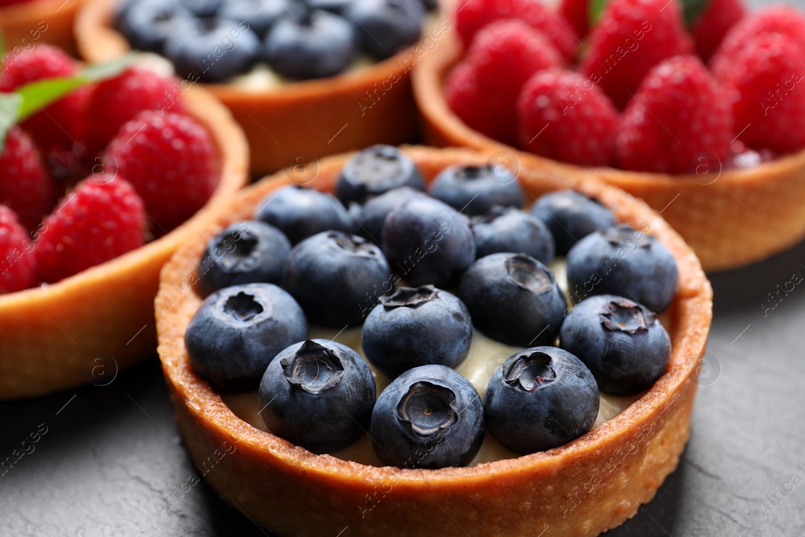 Photo of Tartlet with fresh blueberries on black table, closeup. Delicious dessert