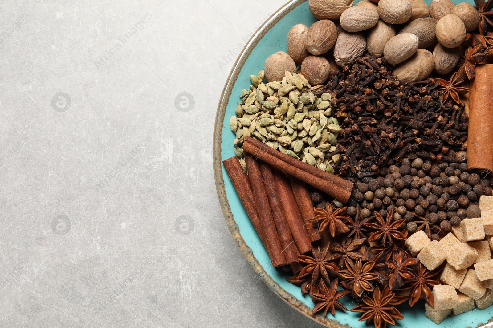 Photo of Different spices and nuts in bowl on light gray textured table, top view. Space for text