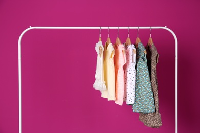 Rack with stylish child clothes on color background