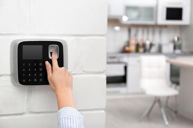 Woman scanning fingerprint on alarm system at home, closeup. Space for text