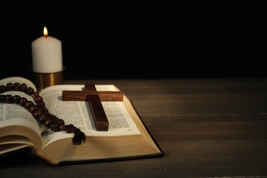 Photo of Church candle, Bible, rosary beads and cross on wooden table, closeup. Space for text