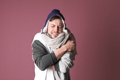 Man in warm clothes suffering from cold on color background