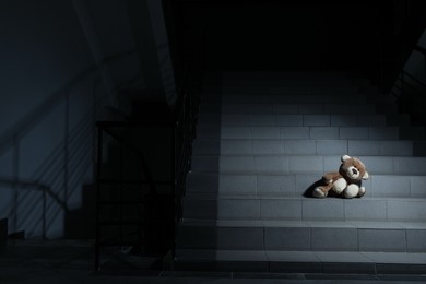 Lonely teddy bear on grey stairs indoors, space for text