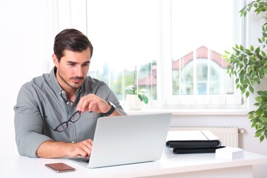 Handsome young man working with laptop at table in office