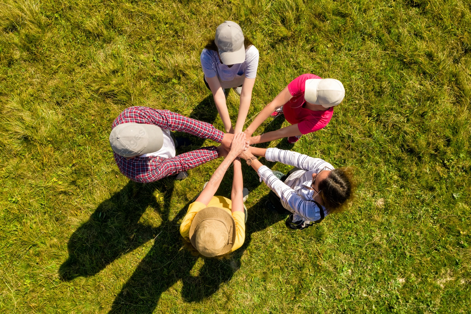 Image of Top aerial view of people holding hands together in circle on green grass. Drone photography