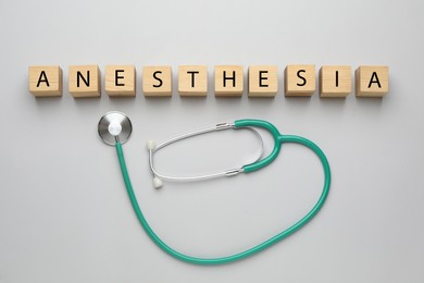 Wooden cubes with word Anesthesia and stethoscope on light grey background, flat lay