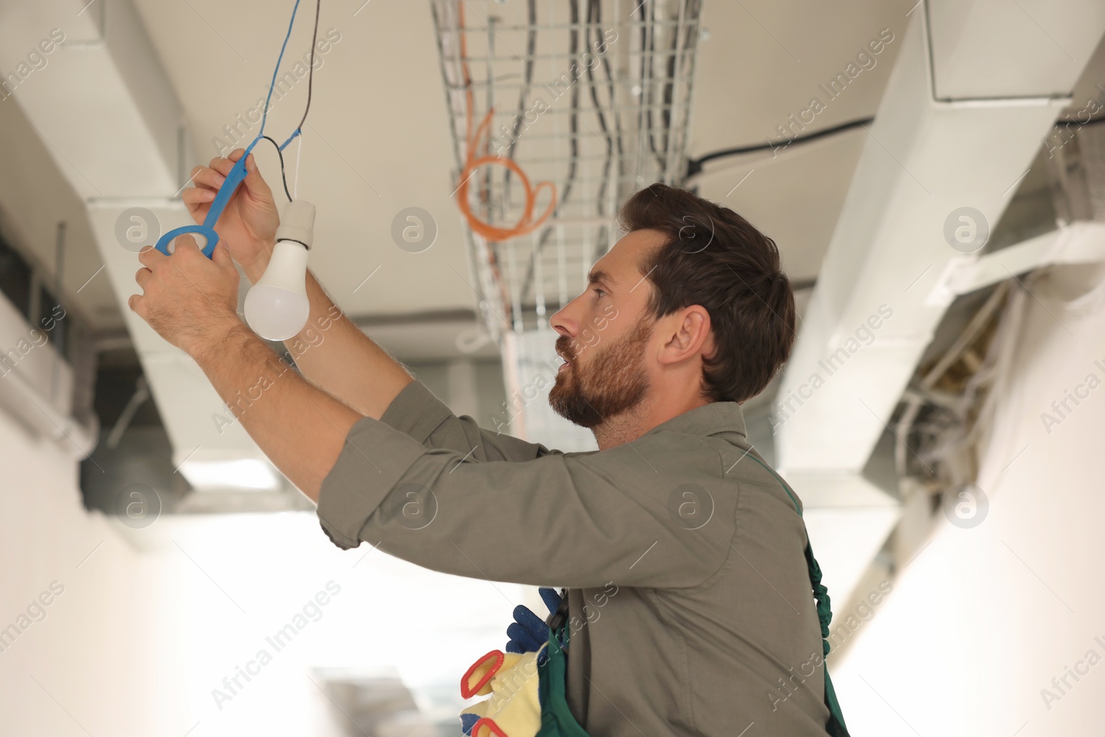 Photo of Electrician with insulting tape repairing ceiling lamp