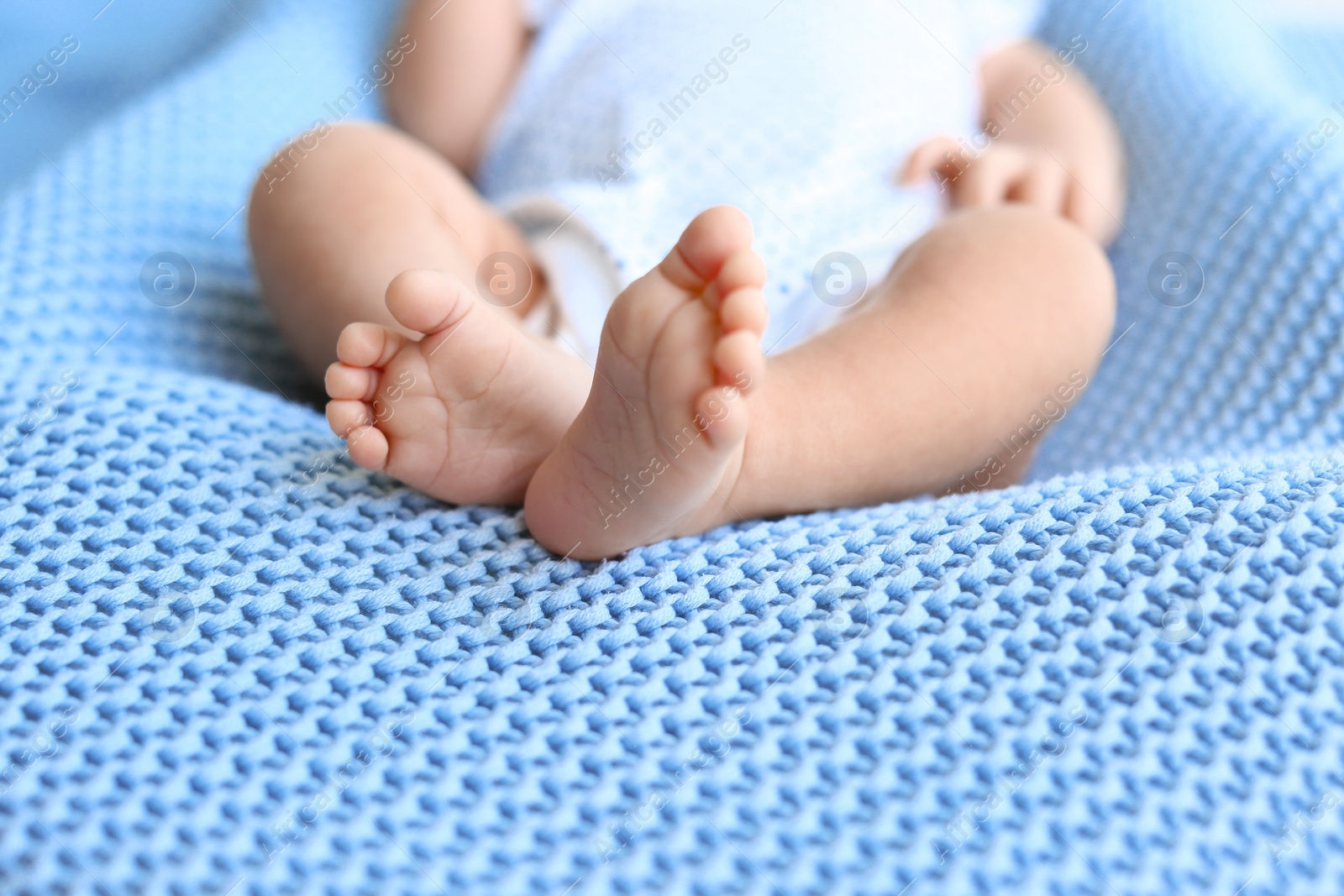 Photo of Cute little baby lying on light blue plaid, closeup