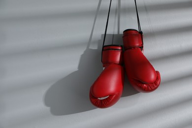 Photo of Pair of red boxing gloves hanging on light wall, space for text