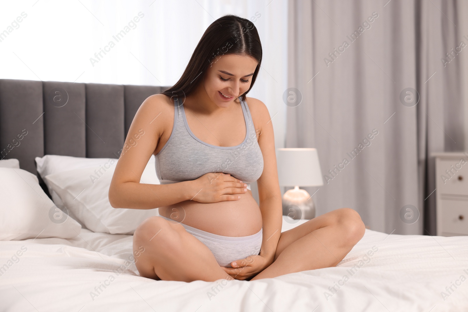 Photo of Beautiful pregnant woman in comfortable maternity underwear on bed at home