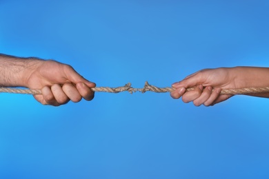 Woman and man pulling damaged rope on color background