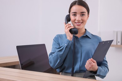 Photo of Female receptionist with clipboard talking on phone at workplace