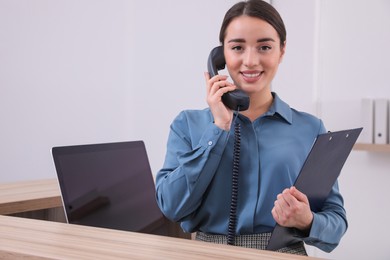 Female receptionist with clipboard talking on phone at workplace