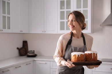 Photo of Young woman with traditional Easter cakes in kitchen, space for text
