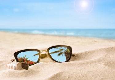 Image of Green palm leaves mirroring in sunglasses on sandy beach with seashell near sea