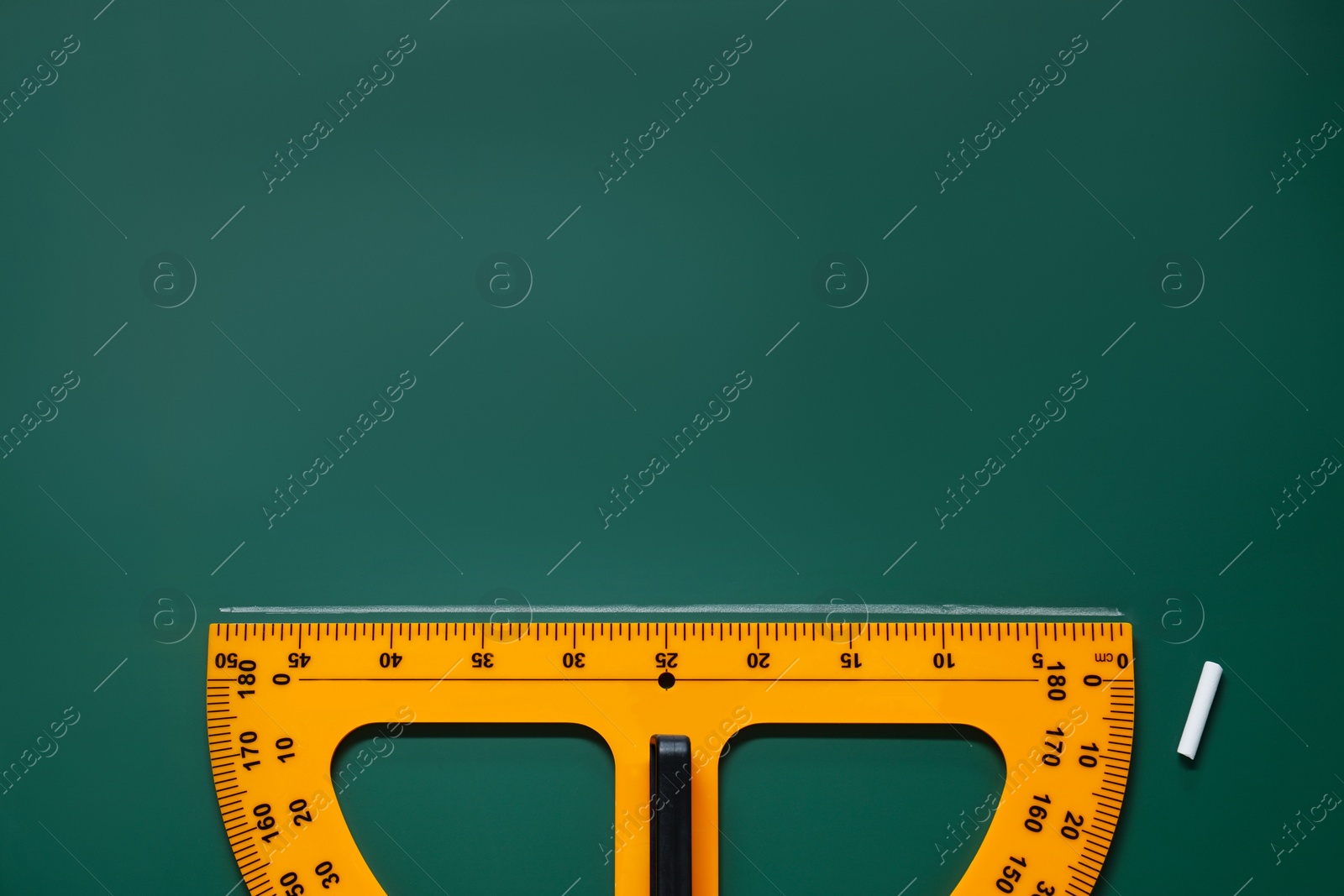 Photo of Yellow protractor and chalk on green chalkboard, flat lay. Space for text