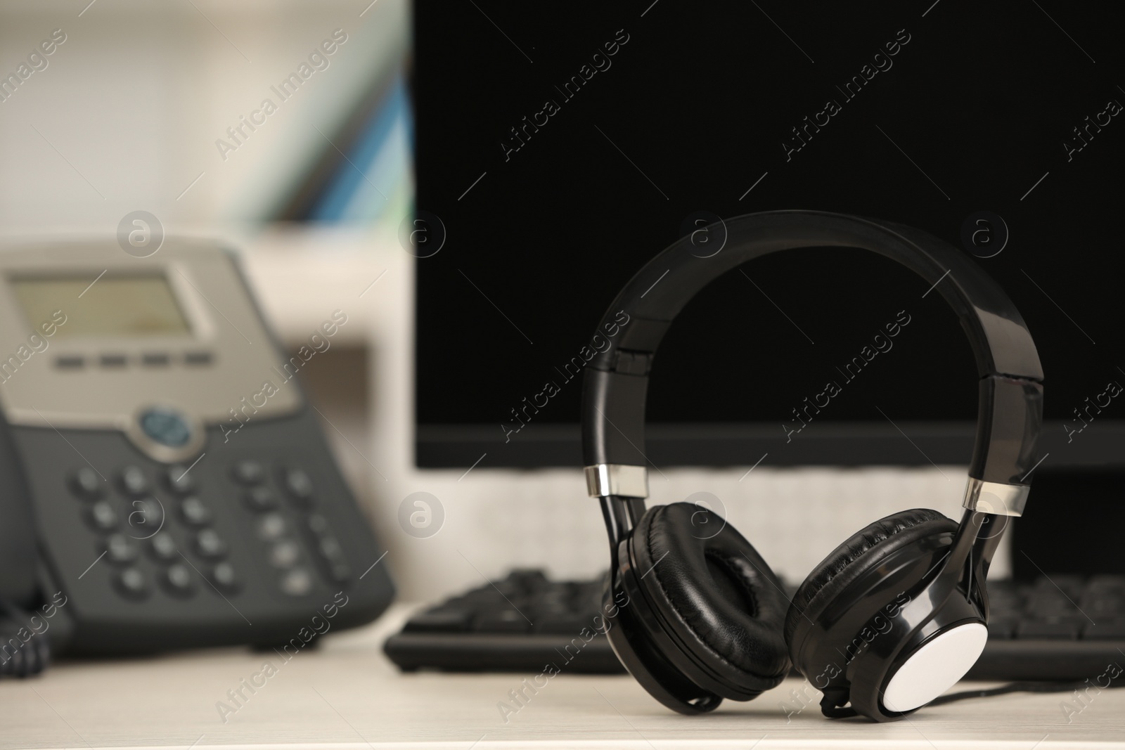 Photo of Modern headphones, desktop telephone and computer on table indoors, space for text