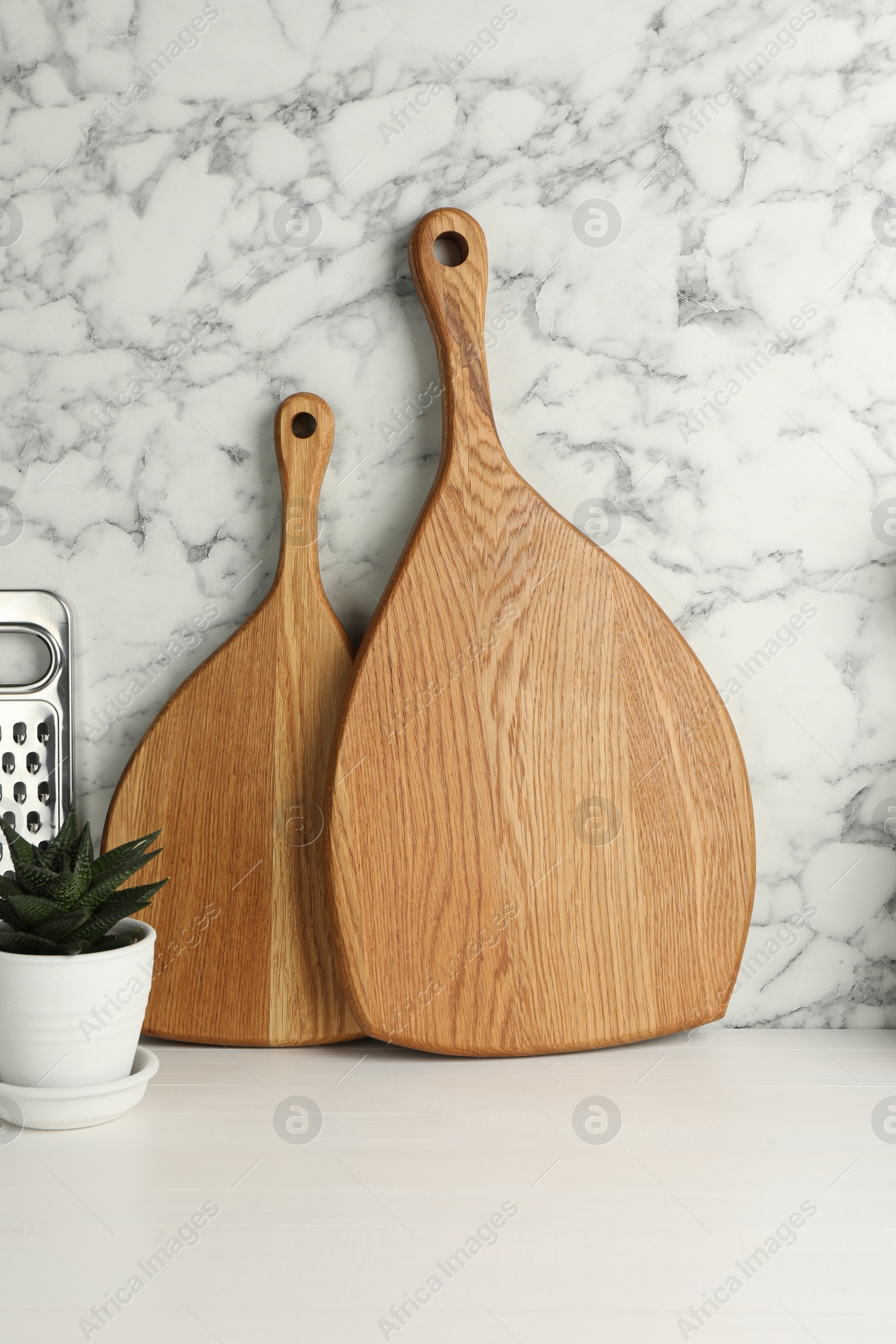Photo of Wooden cutting boards, grater and houseplant on white table near marble wall