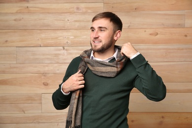 Photo of Handsome young man in warm sweater with scarf on wooden background