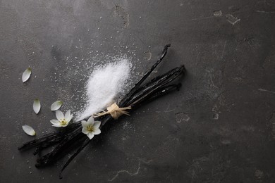 Photo of Vanilla pods, sugar, flowers and petals on gray textured table, flat lay. Space for text